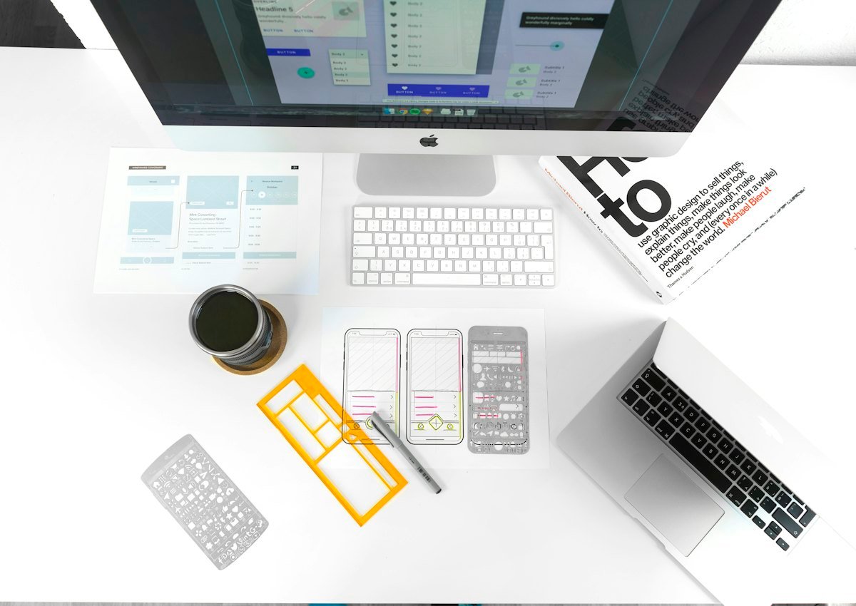 Designer sketching wireframes beside a laptop showing the screens in progress